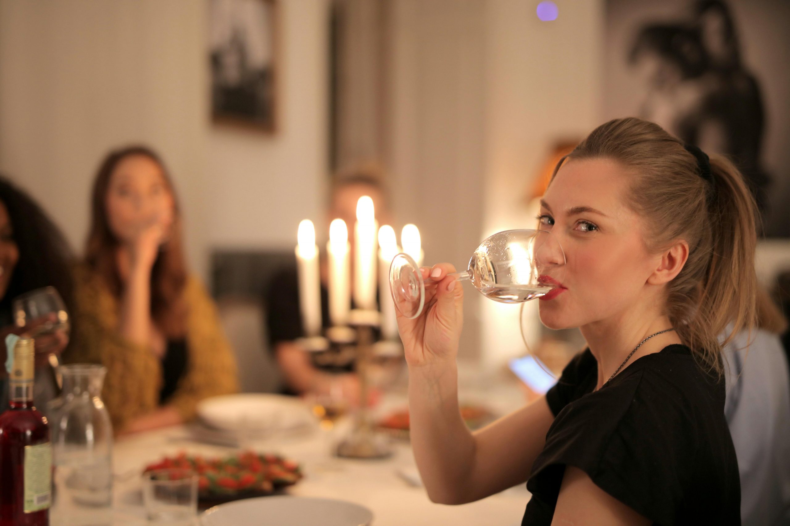 A group enjoys wine and conversation at a cozy candlelit dinner indoors.