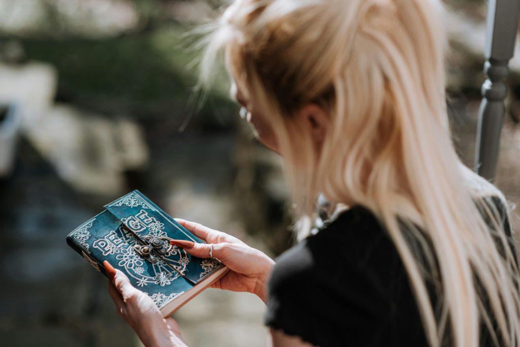 A woman holds an intricately designed journal in an outdoor setting, creating a mysterious and enchanting atmosphere.