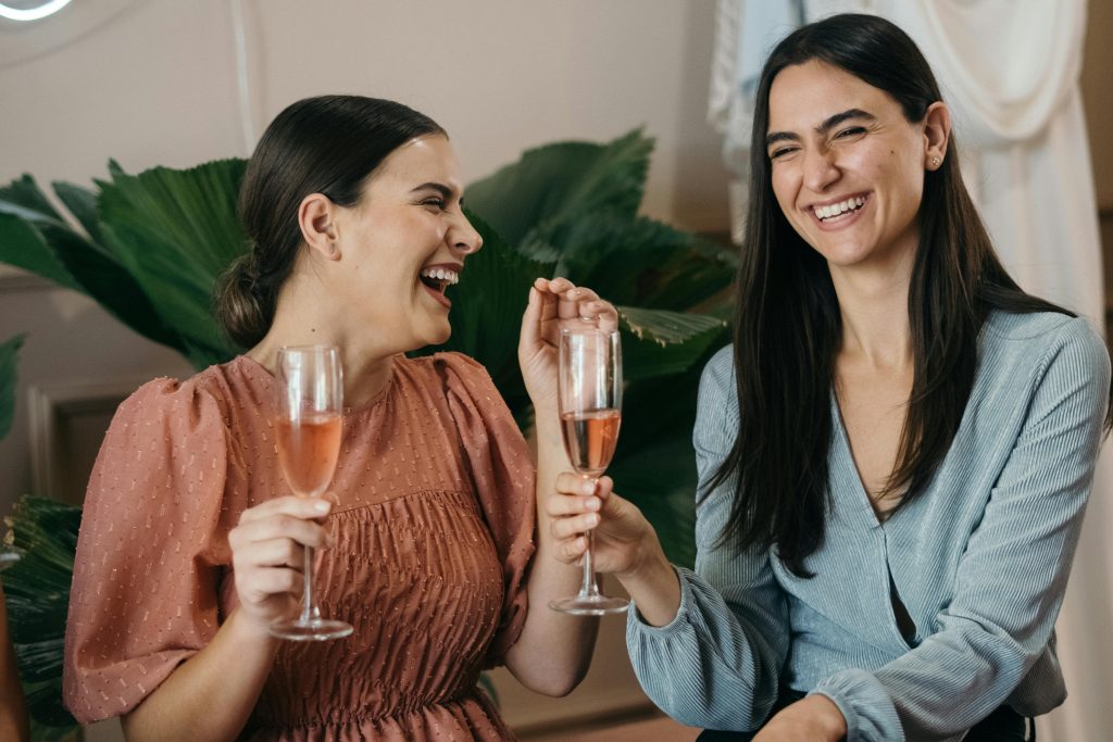 Two women smiling and enjoying rose wine at an indoor celebration.